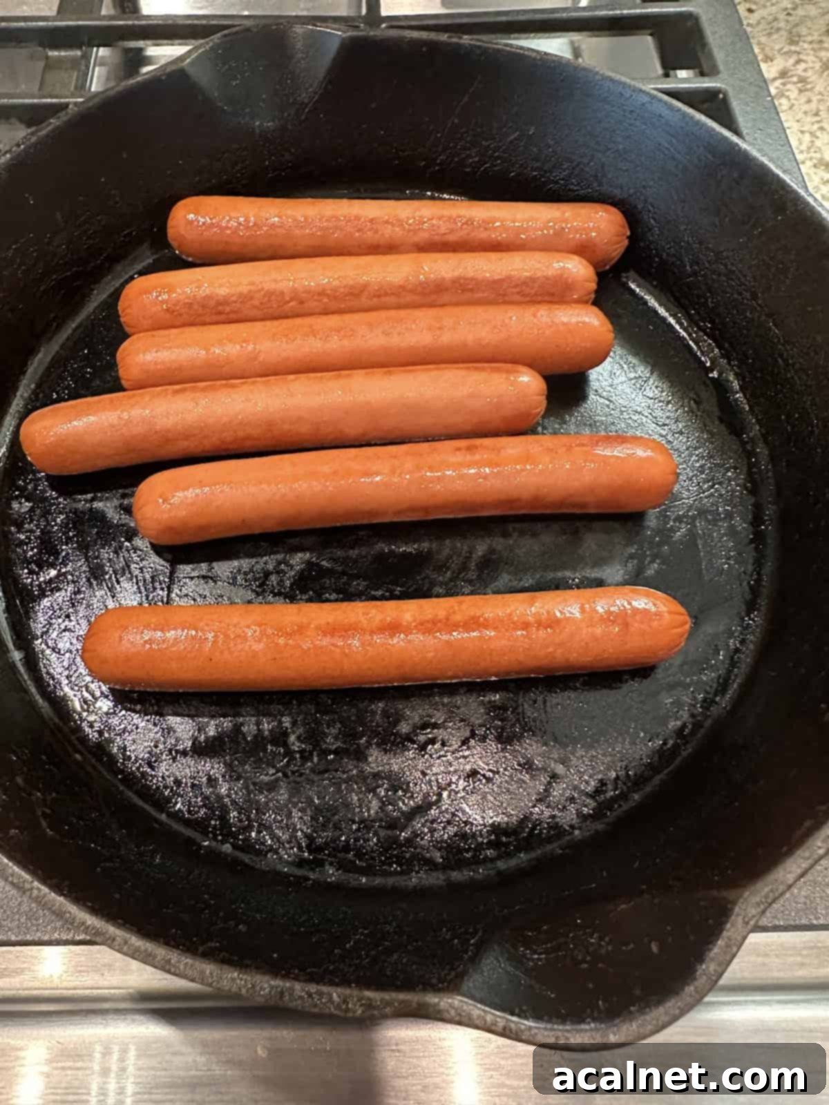 Hotdogs browning in a skillet on the stovetop.