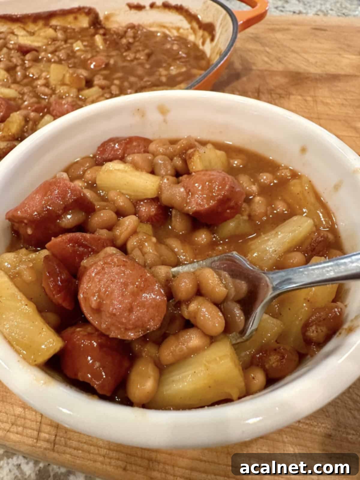 A serving bowl of warm baked beans, hot dogs, and pineapple, ready to be enjoyed.