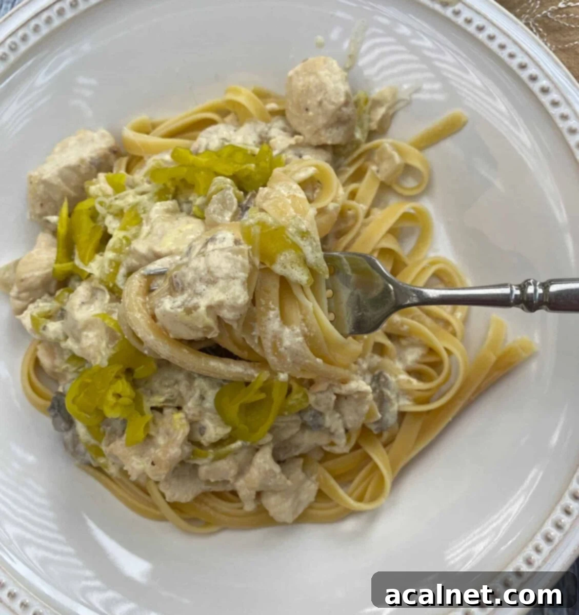 A serving of spicy chicken Alfredo on a plate with a fork that has a scoop of pasta and sauce.