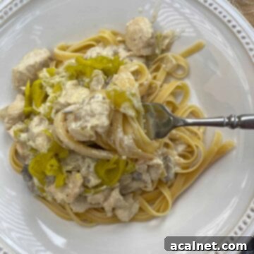 A serving of spicy chicken Alfredo on a plate with a fork that has a scoop of pasta and sauce.