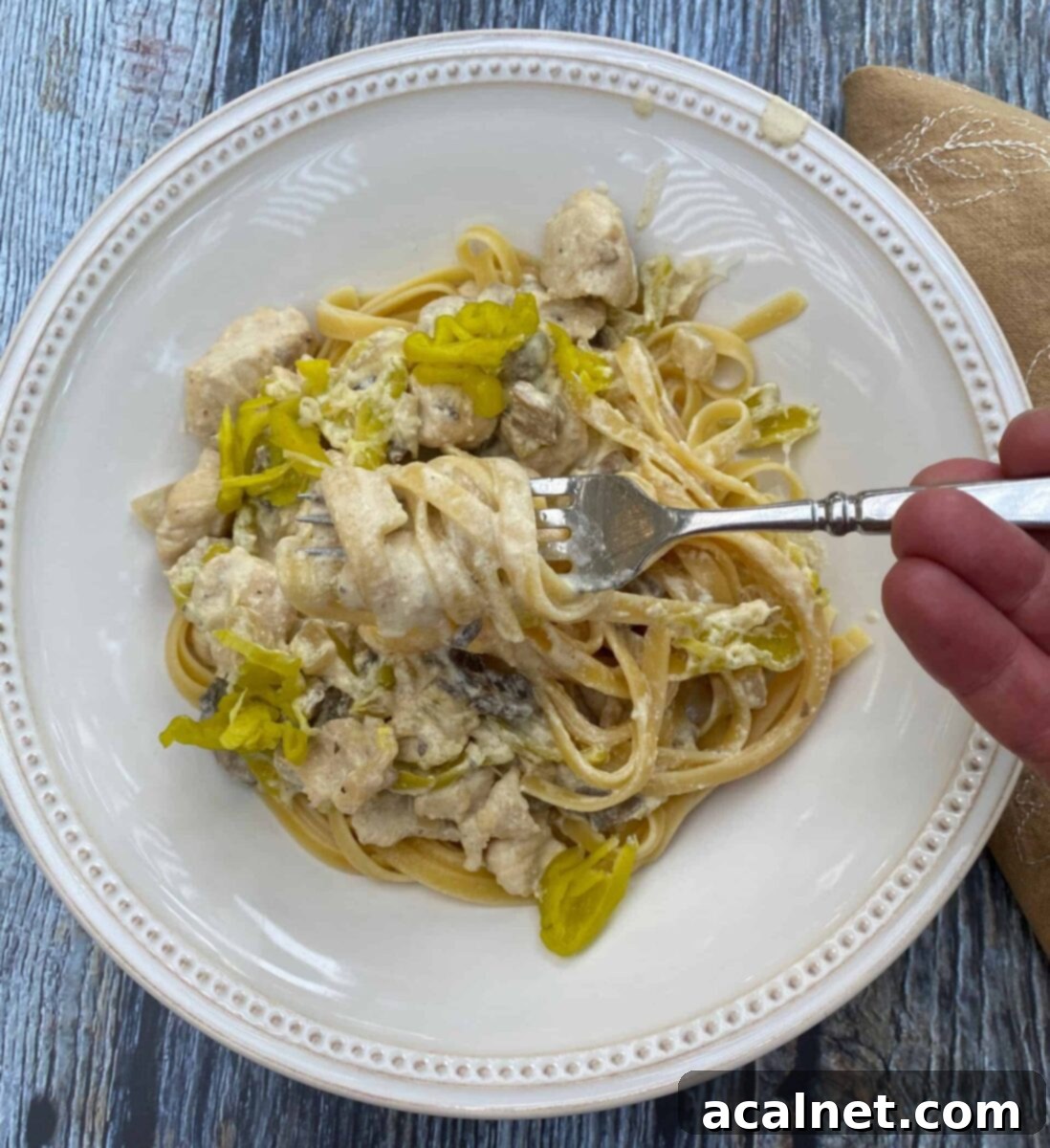 A serving of spicy chicken Alfredo on a plate with a fork and a napkin on the side.