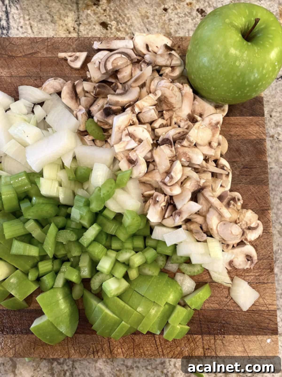 Sweet and Savory Cranberry Apple Stuffing 4 Freshly chopped onions, mushrooms, and diced apples on a wooden cutting board, ready for cooking.