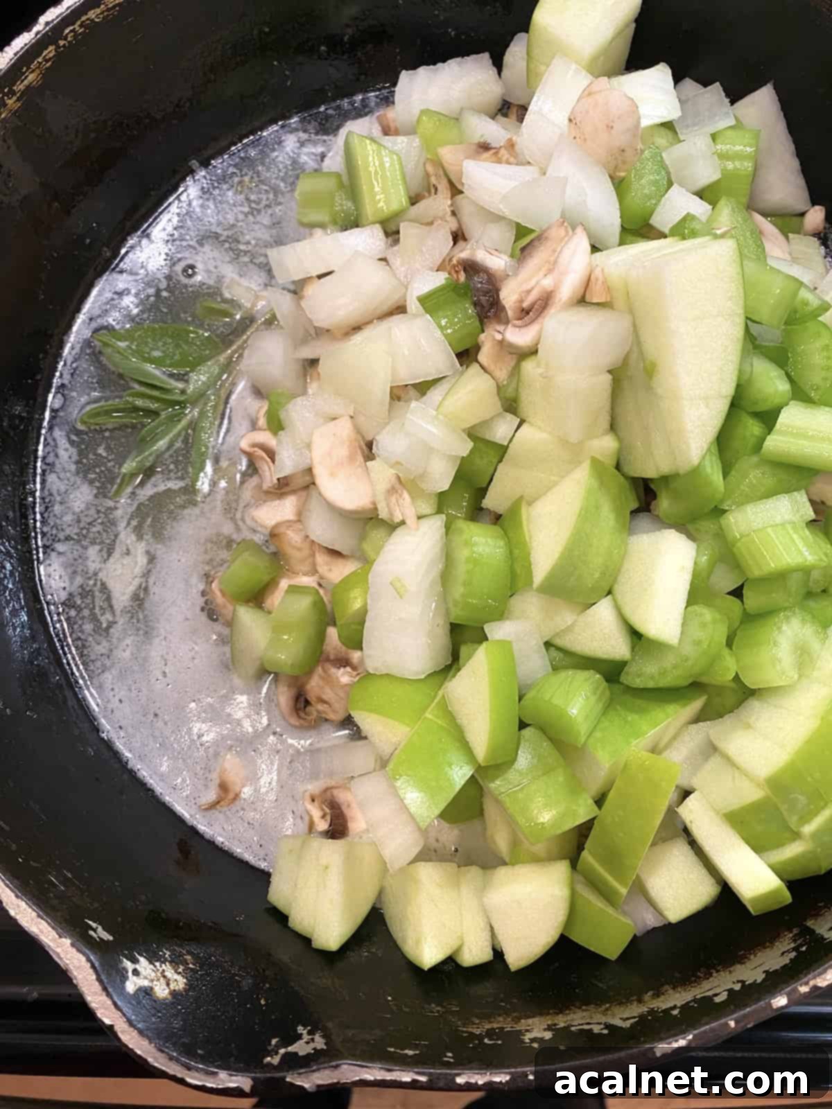 Sweet and Savory Cranberry Apple Stuffing 7 A skillet filled with chopped onions, mushrooms, celery, and apples.