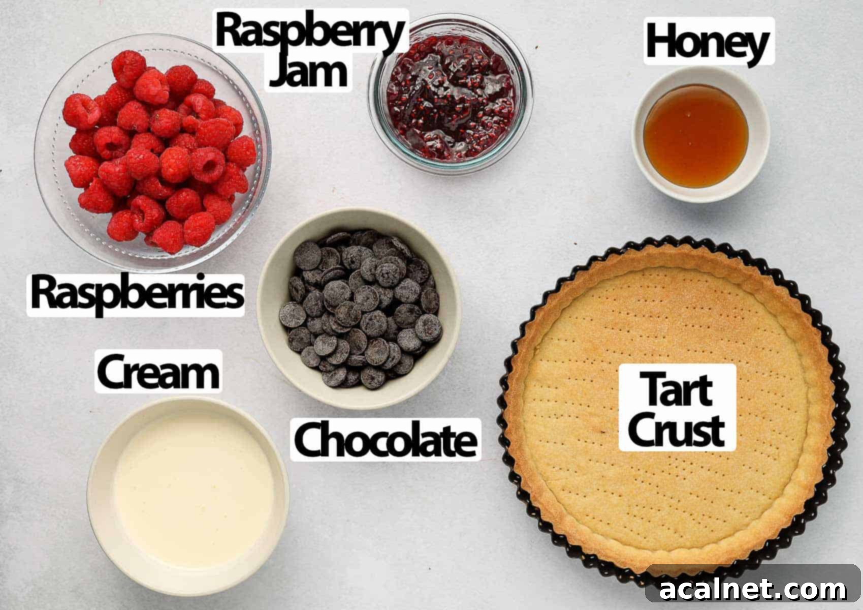 Decadent Chocolate Raspberry Tart 3 Collection of fresh ingredients for chocolate raspberry tart, including flour, sugar, butter, chocolate, cream, and fresh raspberries, arranged on a grey surface.