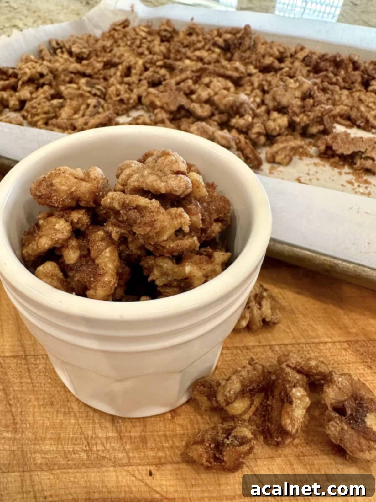 Spiced walnuts in a small jar next to to a baking pan, showcasing their golden, candied coating.