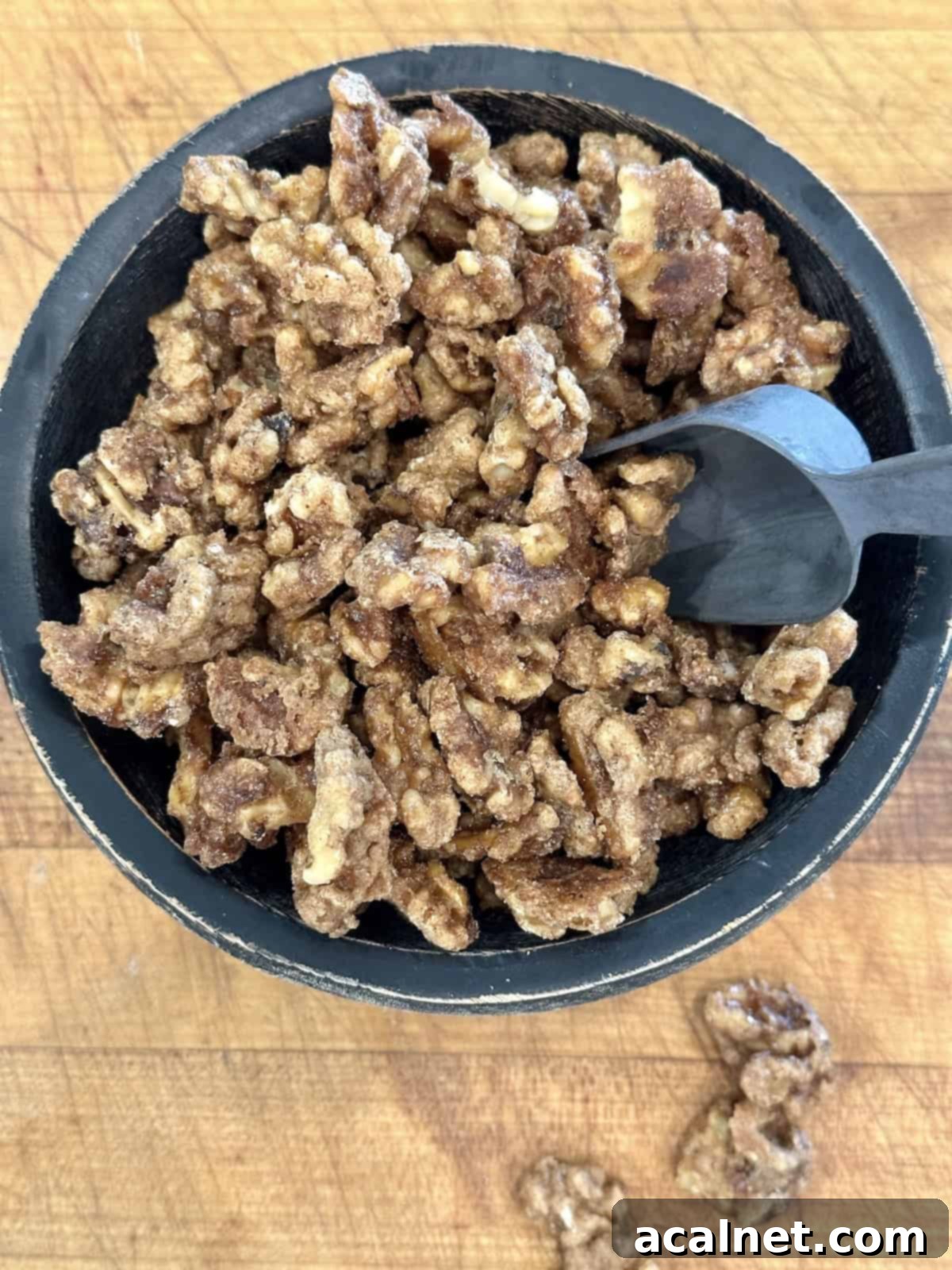 Spiced walnuts in a serving bowl with a small scoop on a cutting board, ready for guests.