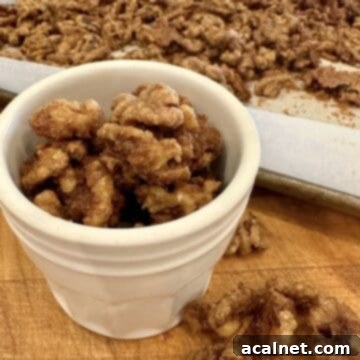 Spiced walnuts in a small jar next to a baking pan, ready to be enjoyed or gifted.