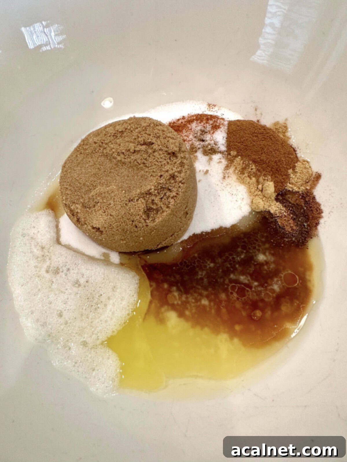 Ingredients for spiced walnuts together in a bowl, showing the foamy egg whites, melted butter, sugars, and spices.