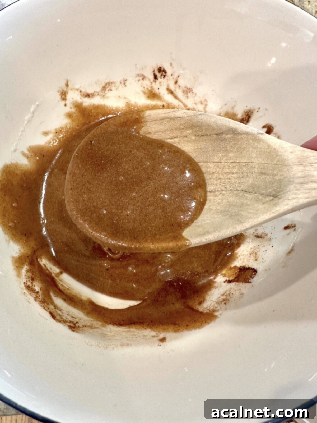 Blended spiced walnuts ingredients in a bowl with a wooden spoon, forming a thick, uniform syrup.