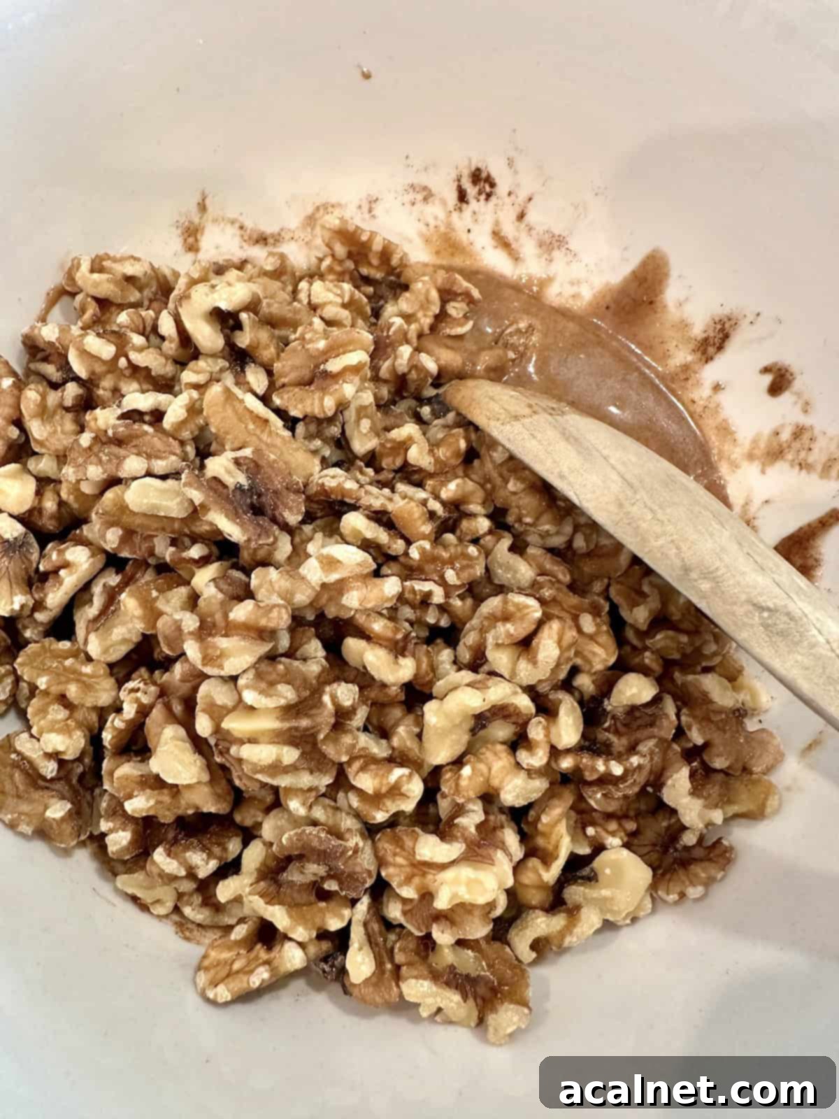 Walnuts fully mixed into the spices and syrup in a bowl, ready for baking.