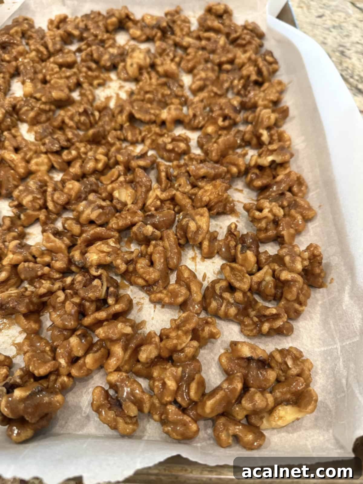 Close-up of spiced walnuts unbaked, coated in spices and syrup, spread evenly on parchment paper.