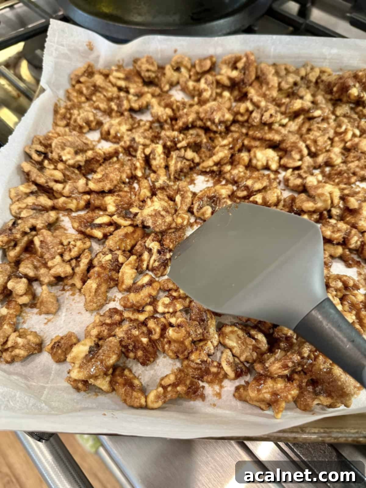 Oven-roasted spiced walnuts partially cooled on parchment paper, with a spatula in the background, showing their golden hue.