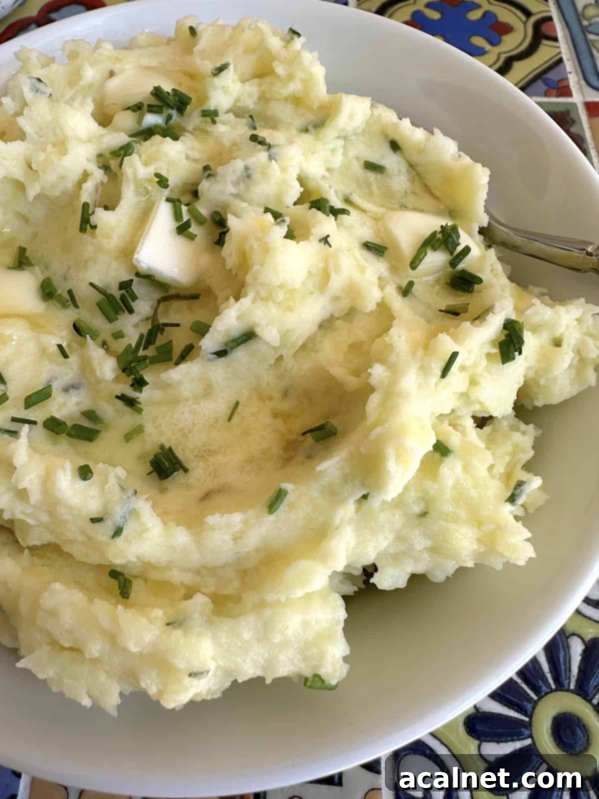 A beautiful bowl of creamy Yukon Gold mashed potatoes, garnished with fresh chives and melted butter.