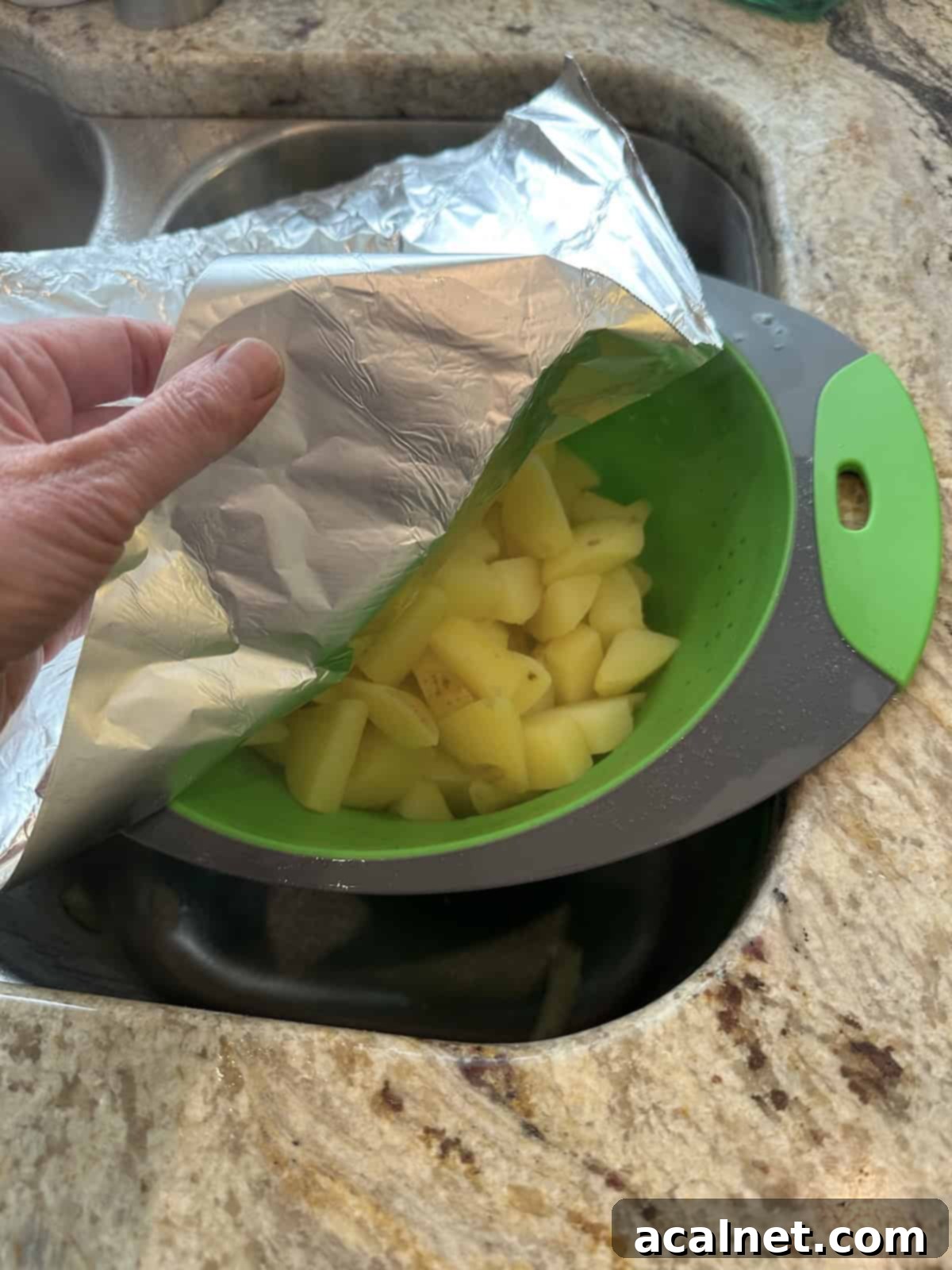 Cooked, drained potatoes steaming in a colander placed over a sink.