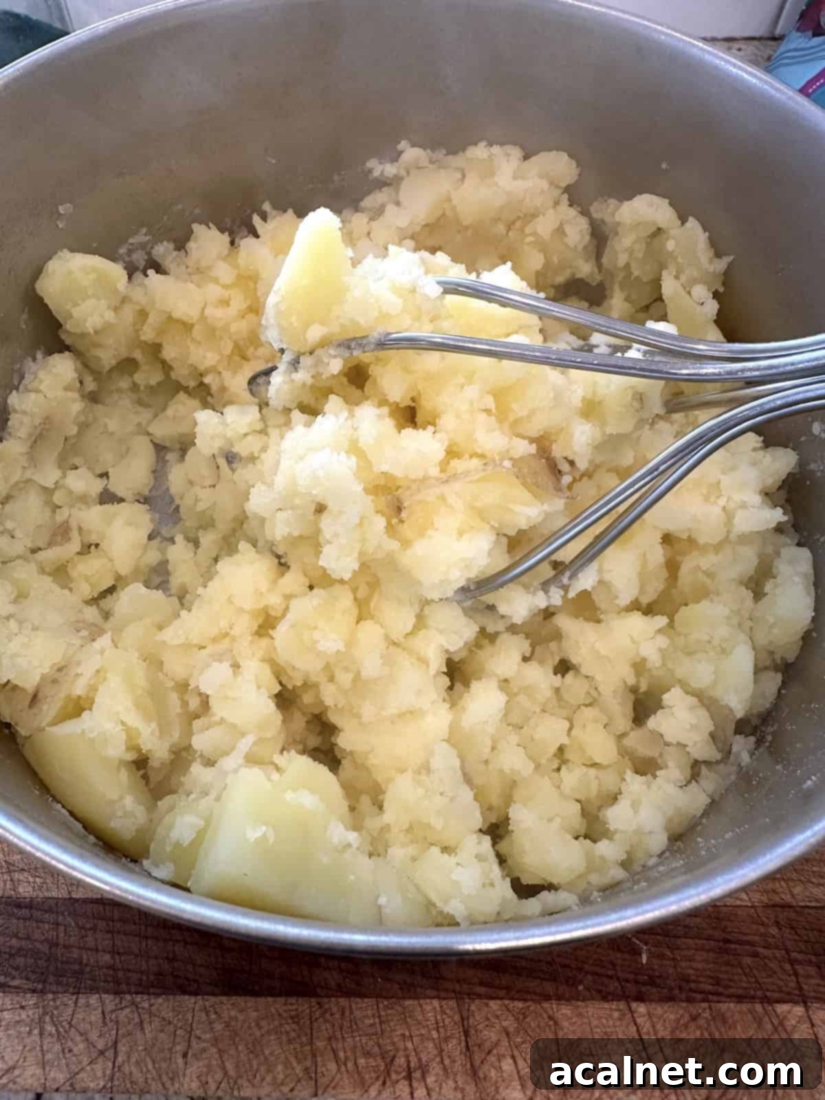 Potatoes being mashed in a pan using a potato masher.