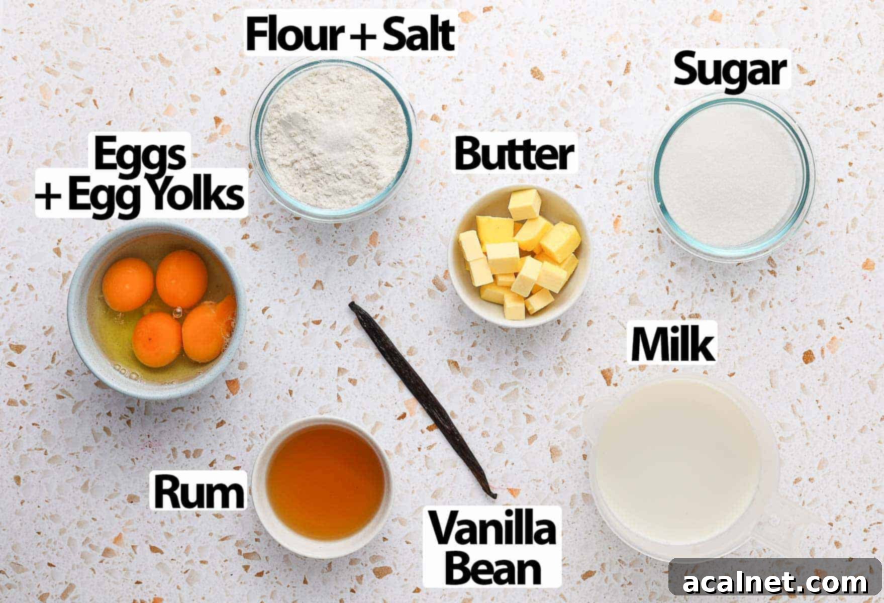 Bordeaux Cannelés 3 Collection of fresh ingredients for Cannelés, including milk, butter, vanilla bean, eggs, sugar, flour, and rum, laid out on a white and orange surface.