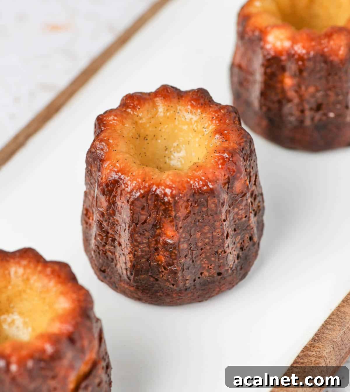 Bordeaux Cannelés 6 Three perfectly golden-brown Cannelés arranged on a long white serving board, ready to be enjoyed.