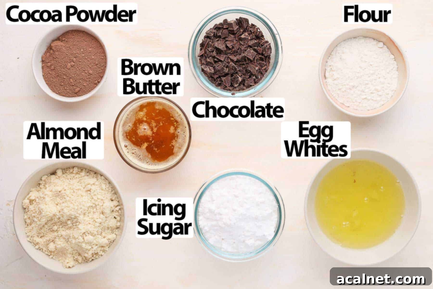 Decadent Chocolate Financiers 3 A flat lay of the essential ingredients for making chocolate financiers: butter, dark chocolate, almond meal, flour, icing sugar, cocoa powder, and egg whites, arranged neatly on a light orange surface.