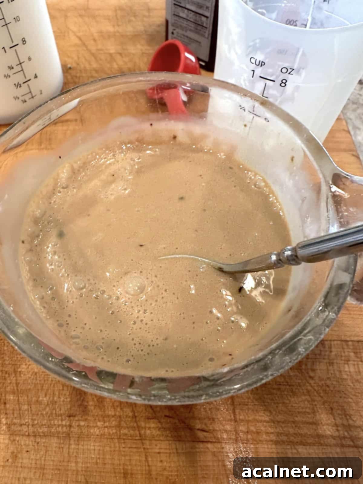 Hot water, instant espresso powder, heavy cream, and sweetened condensed milk being mixed in a glass measuring cup.