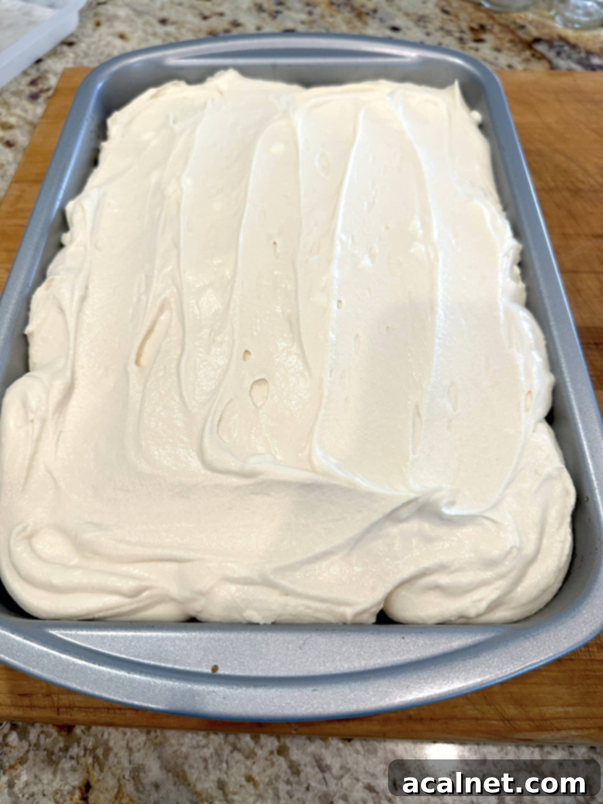Mascarpone frosting smoothly spread over the top of the tiramisu cake in a baking dish, creating an even layer.