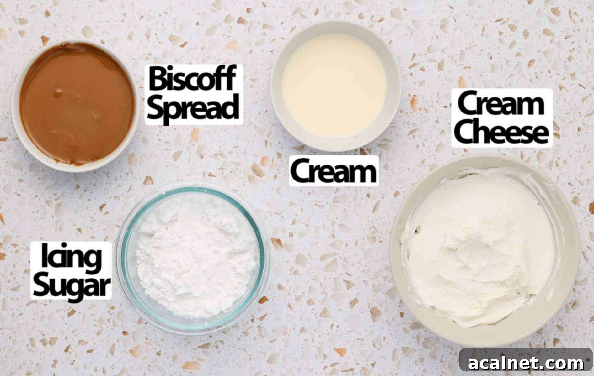 Four key ingredients - cream cheese, biscoff spread, icing sugar, and heavy cream - arranged neatly on a light speckled surface.
