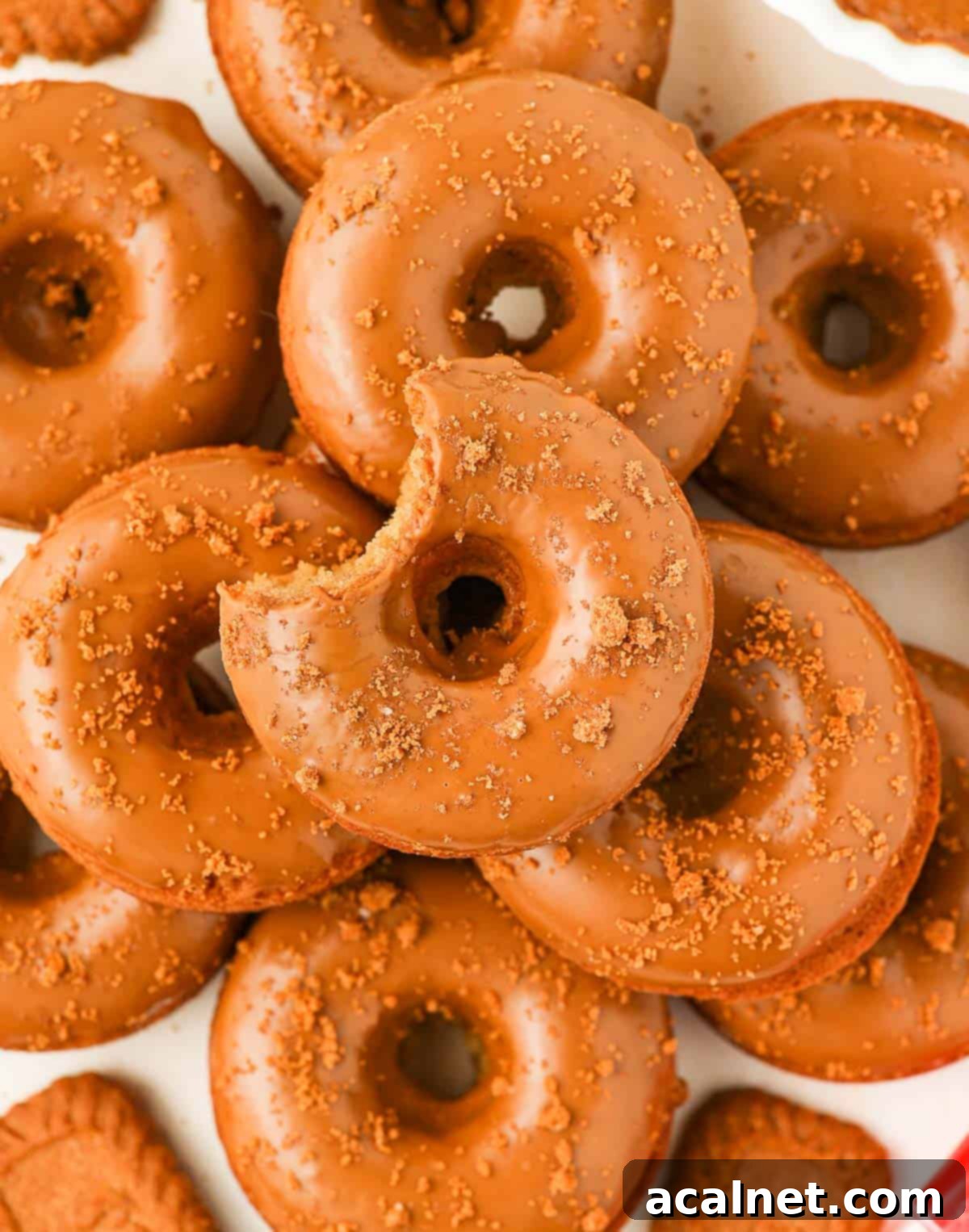 A stack of perfectly glazed Biscoff donuts, viewed from above, with crumbs scattered around.