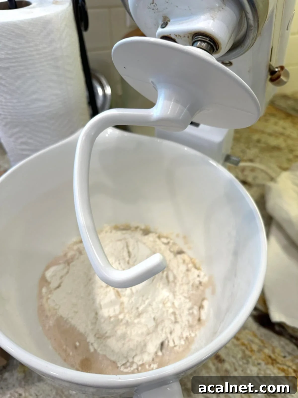 Pizza dough ingredients in a mixer with a dough hook.