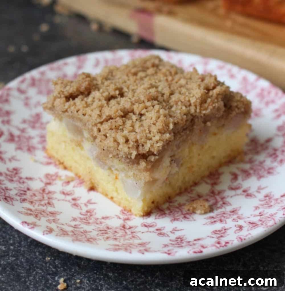 Slice of Pear Crumble Cake on a white and pink plate, showing the moist cake, pear chunks, and crunchy streusel topping.