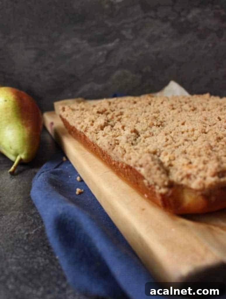 Whole baked Pear Crumble Cake on a rustic wooden cutting board, with a slight dusting of powdered sugar, ready to be sliced and served.