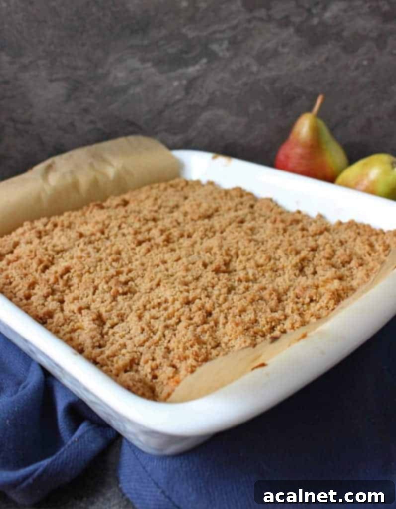 Whole Pear Crumble Cake in a white ceramic baking dish, garnished with fresh pears on a navy napkin, showcasing its rustic charm and golden streusel.