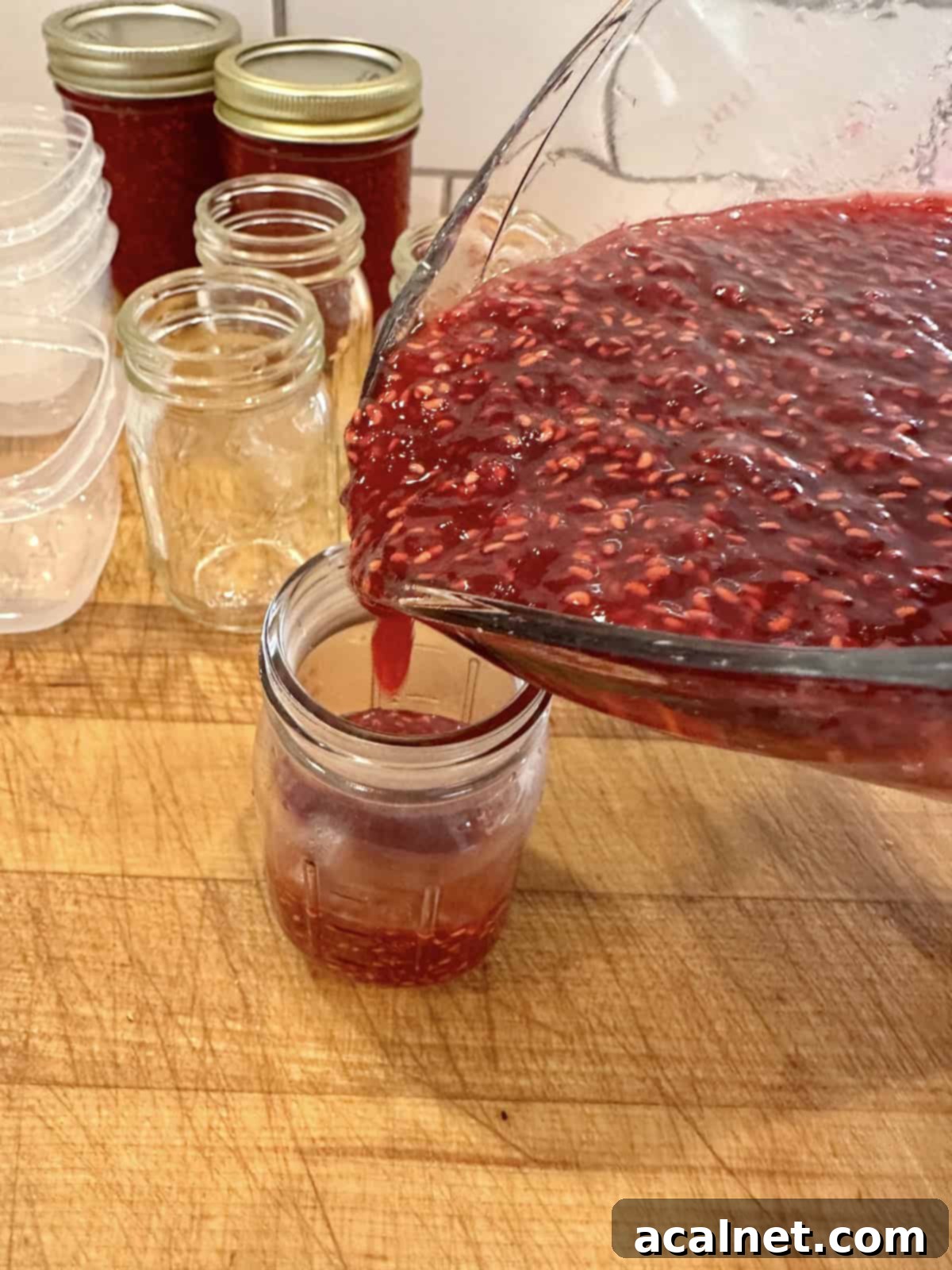 A small jar being filled with raspberry jam.
