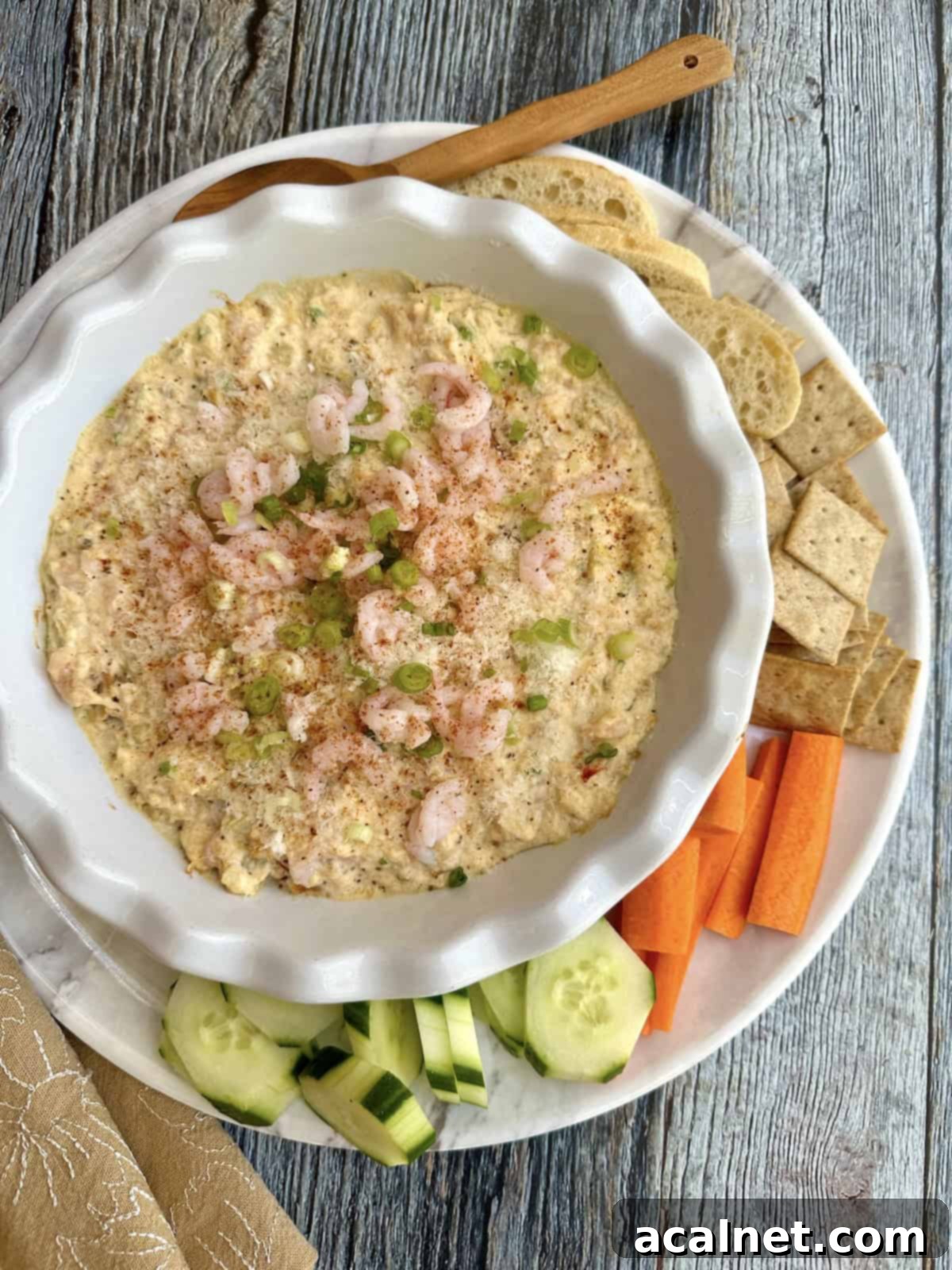 Irresistible Crab and Shrimp Dip 2 A platter with a warm, bubbling crab and shrimp dip in a ceramic dish, surrounded by fresh vegetables like cucumber and carrots, and an assortment of crackers.