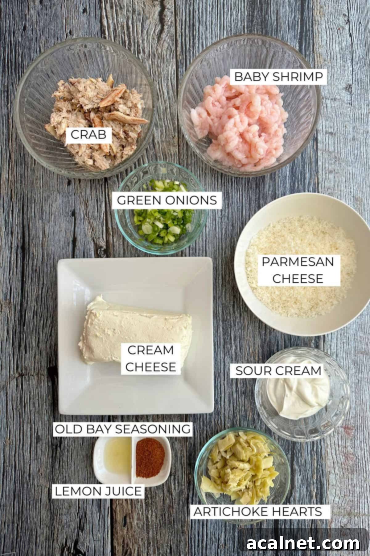 Irresistible Crab and Shrimp Dip 4 Various ingredients for shrimp and crab dip laid out on a rustic wooden table, including cream cheese, sour cream, canned artichokes, Old Bay seasoning, lemon, green onions, and fresh seafood.