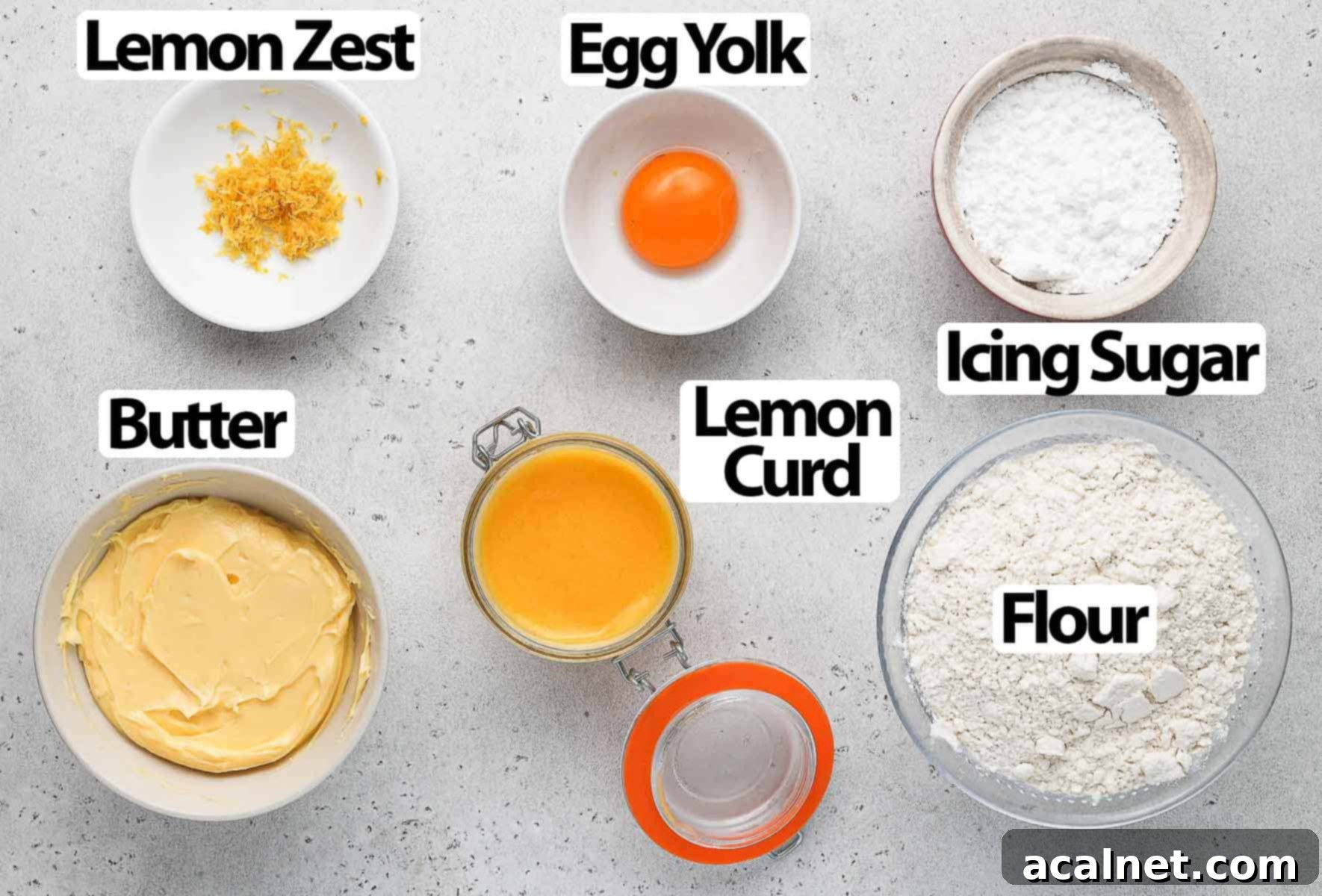 Fresh ingredients for lemon curd cookies, including butter, flour, eggs, and lemons, arranged on a grey surface.