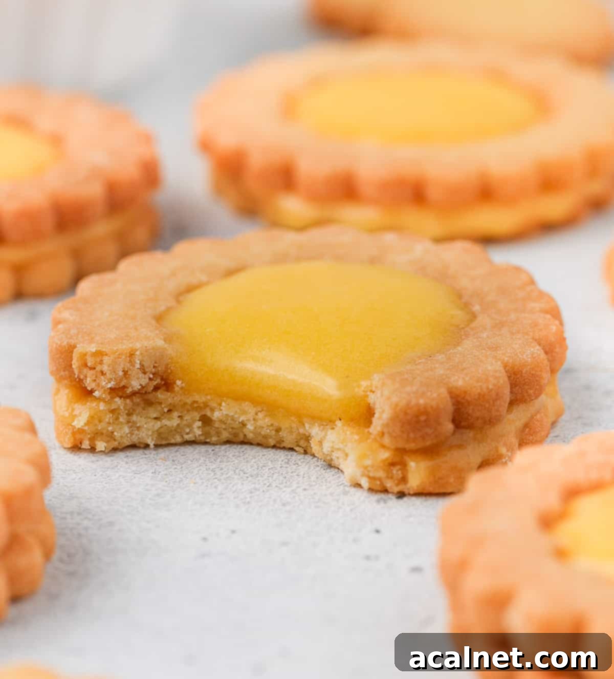 Close-up of a lemon curd cookie with a bite taken out, showing the buttery shortbread and zesty filling.