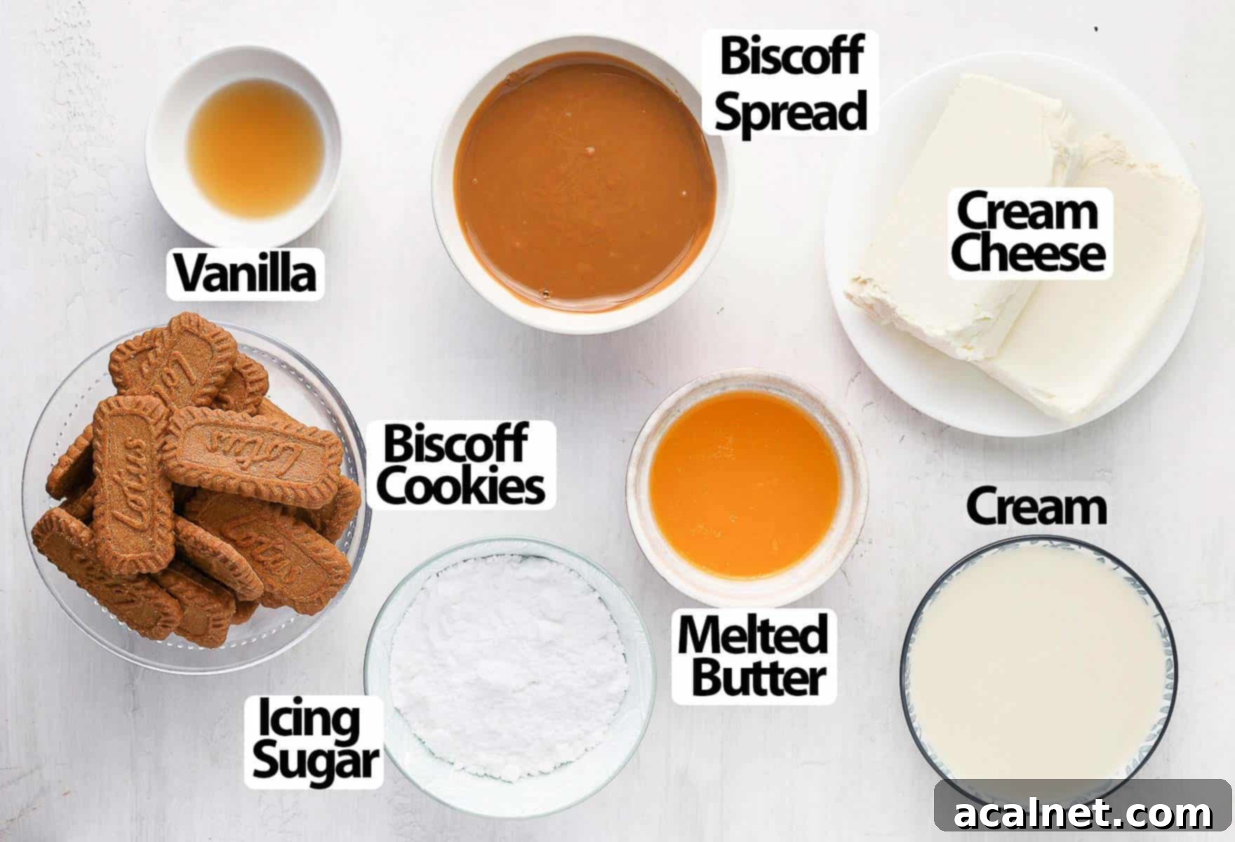 Effortless Biscoff Cheesecake Bliss 3 A selection of ingredients laid out on a light grey surface, including Biscoff cookies, cream cheese, butter, Biscoff spread, icing sugar, and cream.