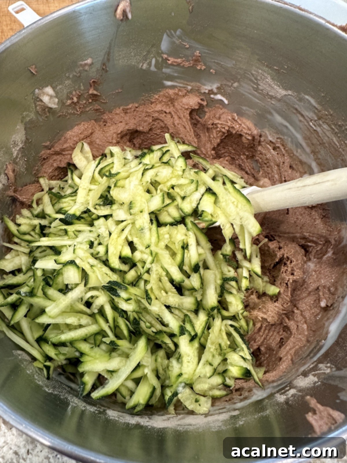 Grated zucchini being folded into the chocolate cake batter in a bowl.