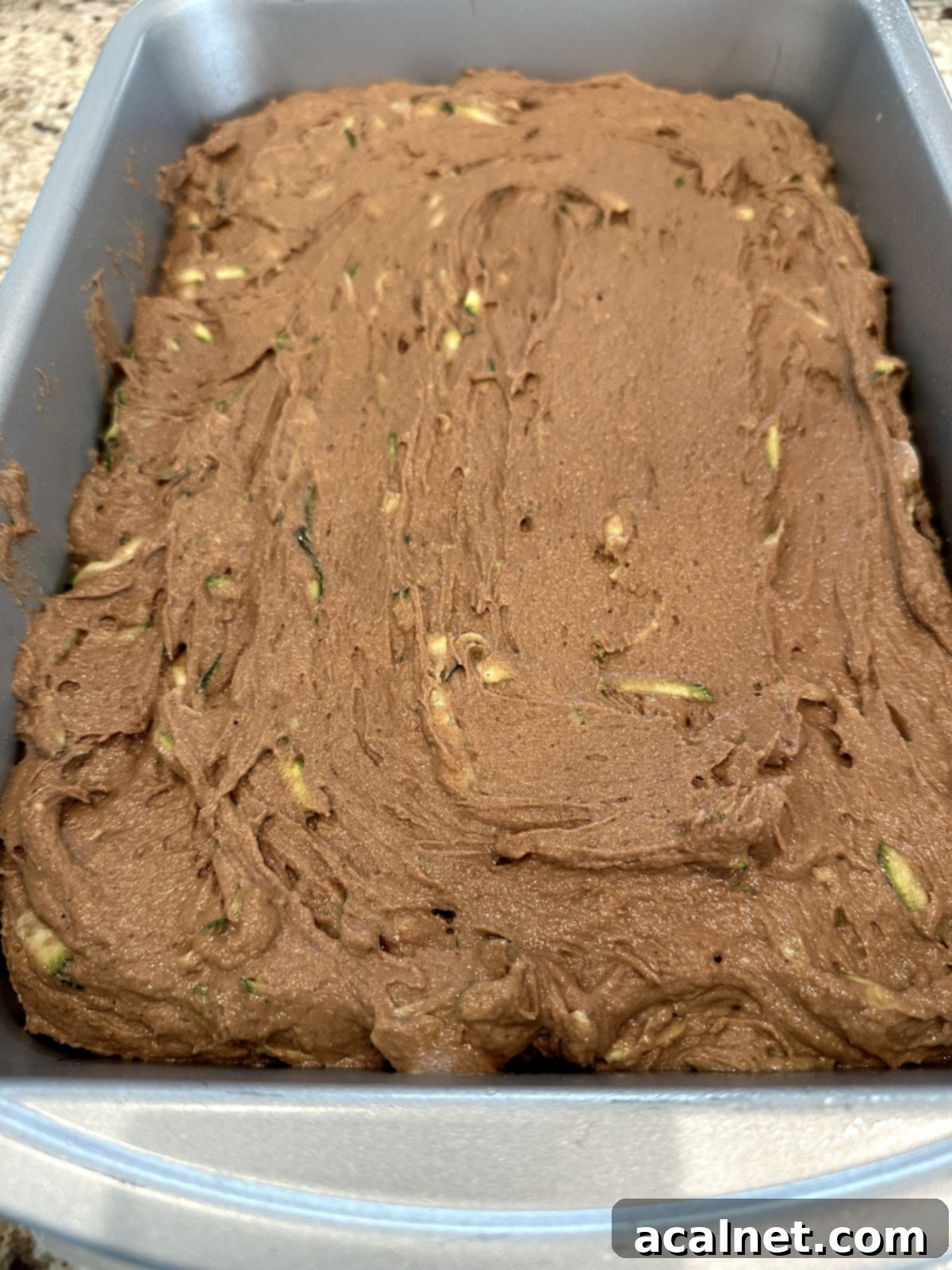 Moist chocolate zucchini cake batter spread evenly in a rectangular baking dish.