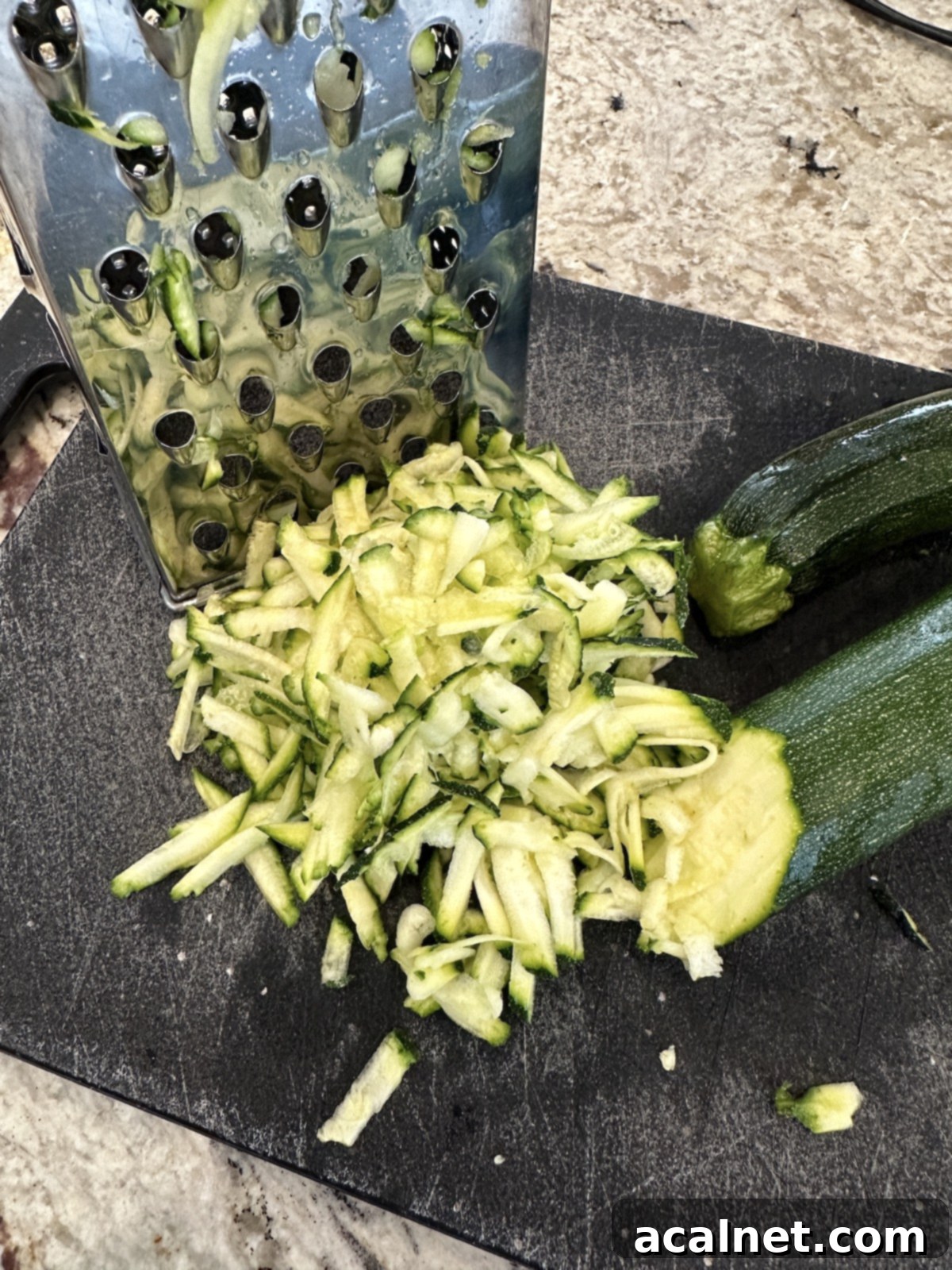 Grated zucchini on a cutting board, ready for moisture removal.