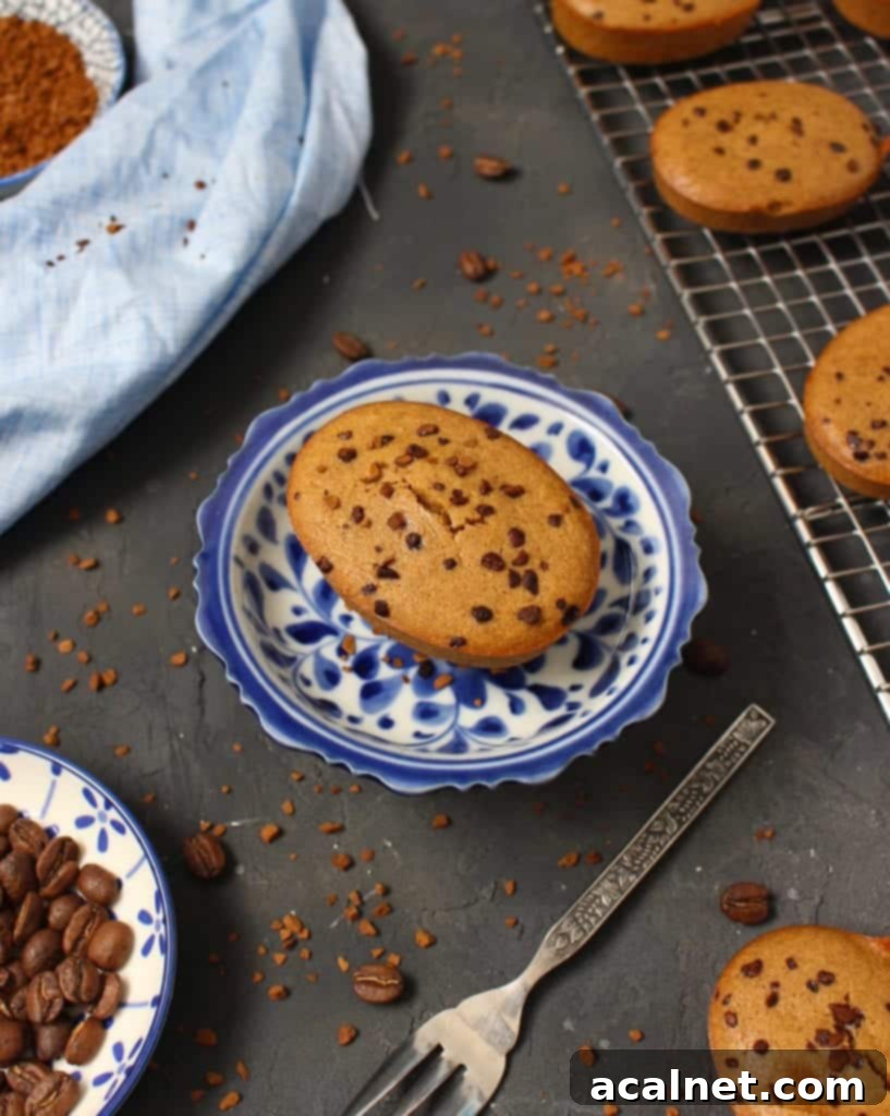 A single coffee financier cake on a white and blue stand, beautifully presented amongst scattered coffee beans, emphasizing its delicious coffee flavor profile.