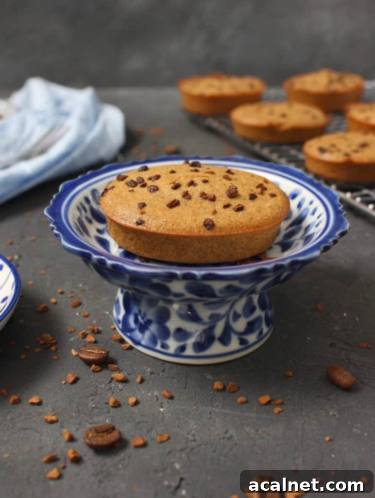 An elegantly styled coffee financier cake on a small white and blue mini stand, highlighting its perfect oval shape and inviting texture, making it an ideal treat for any coffee enthusiast.