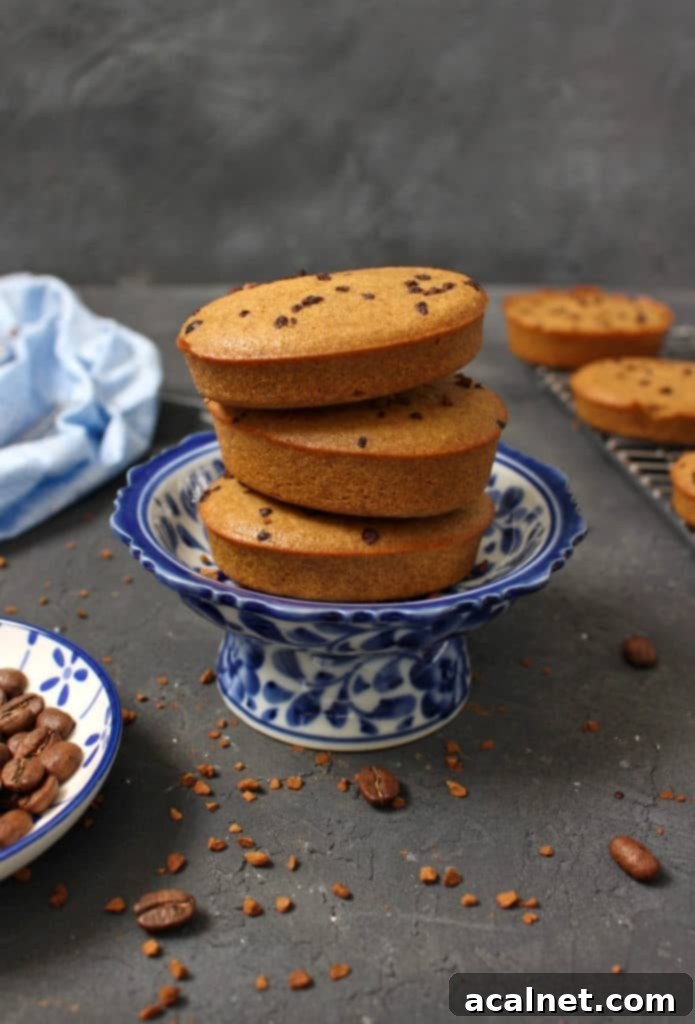 Three perfectly baked coffee financiers stacked over a delicate blue mini cake stand, their golden-brown color and inviting aroma suggesting a delightful experience.