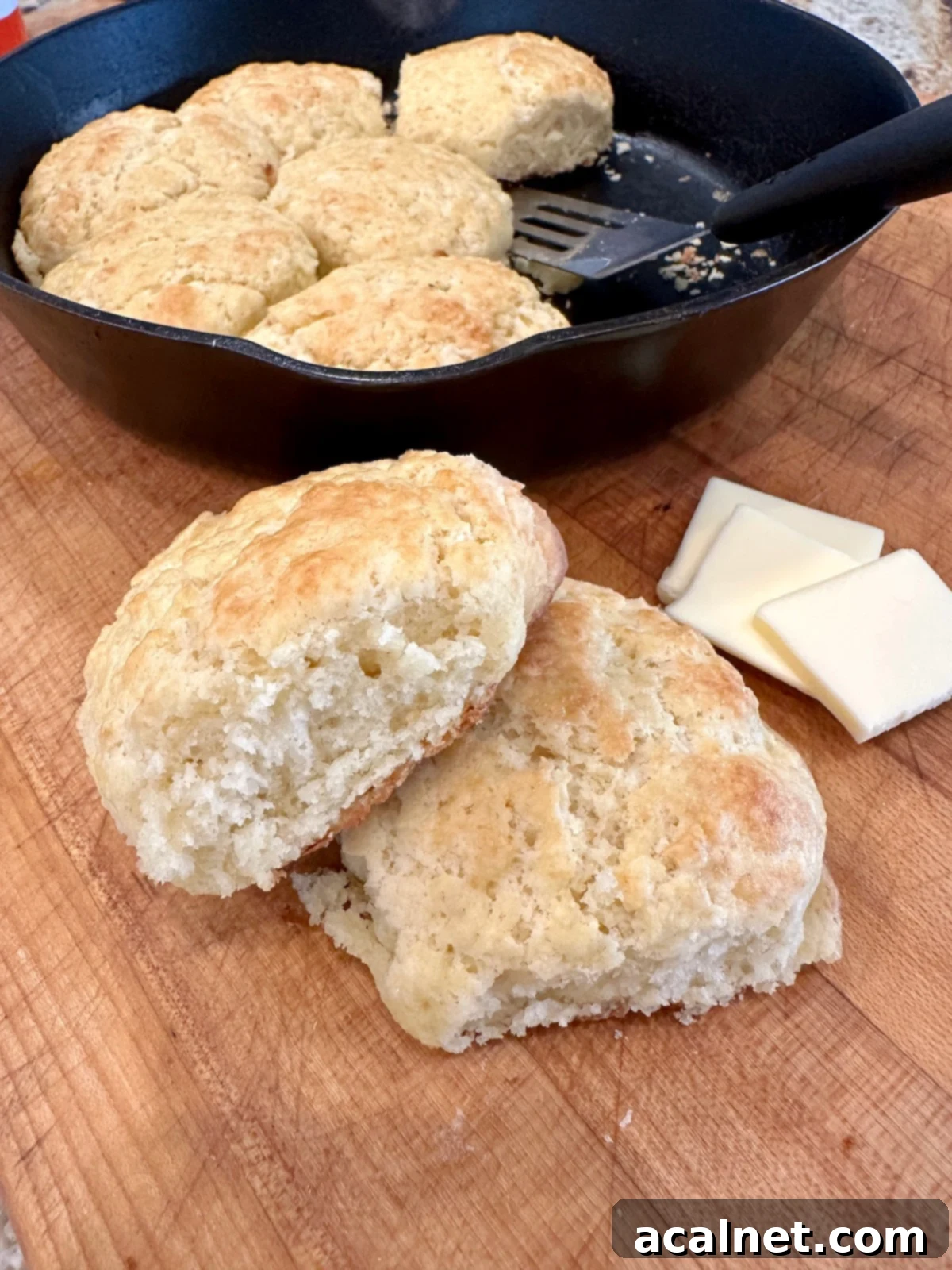 Baked homemade biscuits on a cutting board with butter, highlighting their golden brown tops and flaky texture.