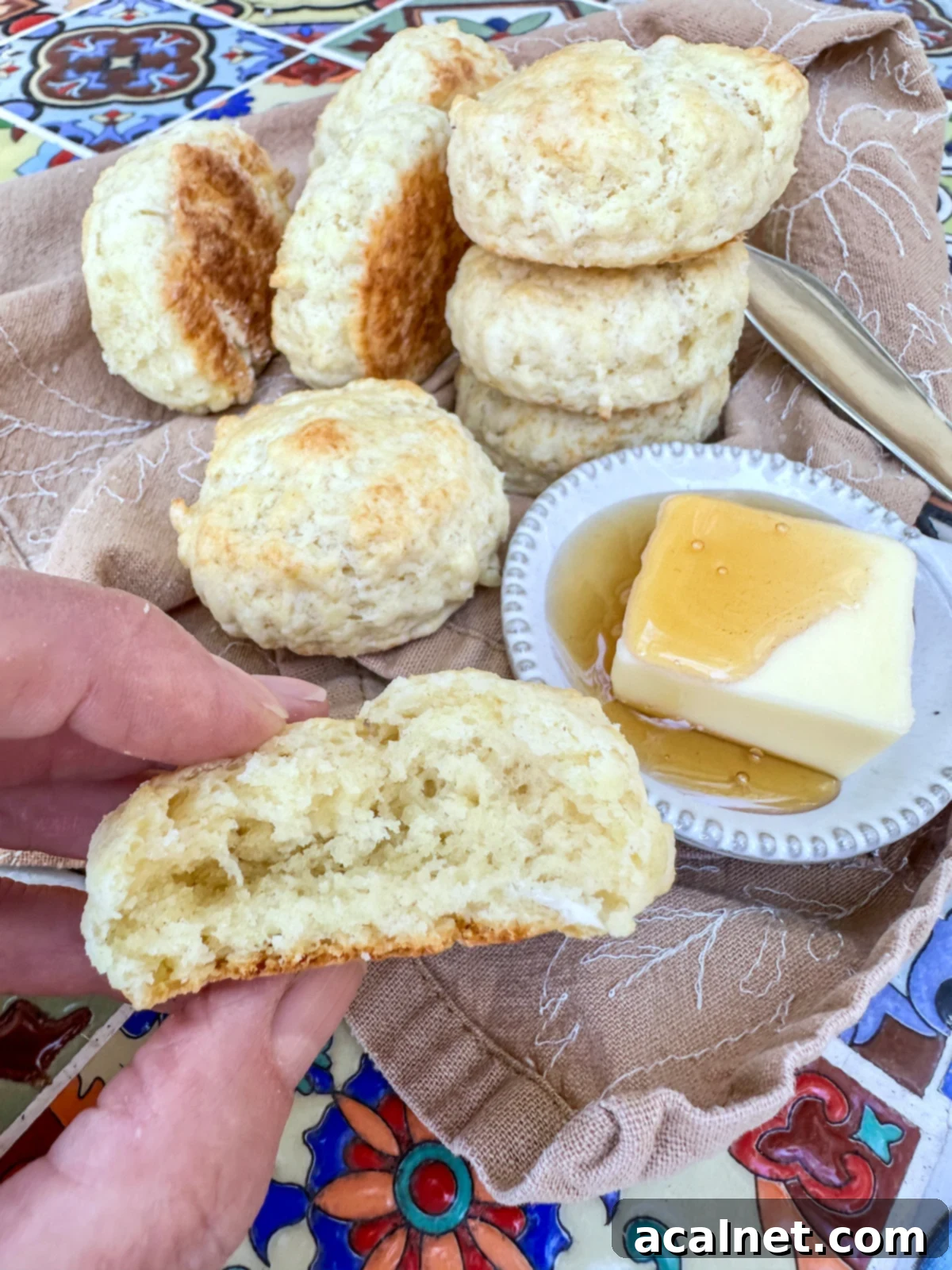 A homemade biscuit cut in half, revealing its tender, flaky interior, with butter and honey on top.