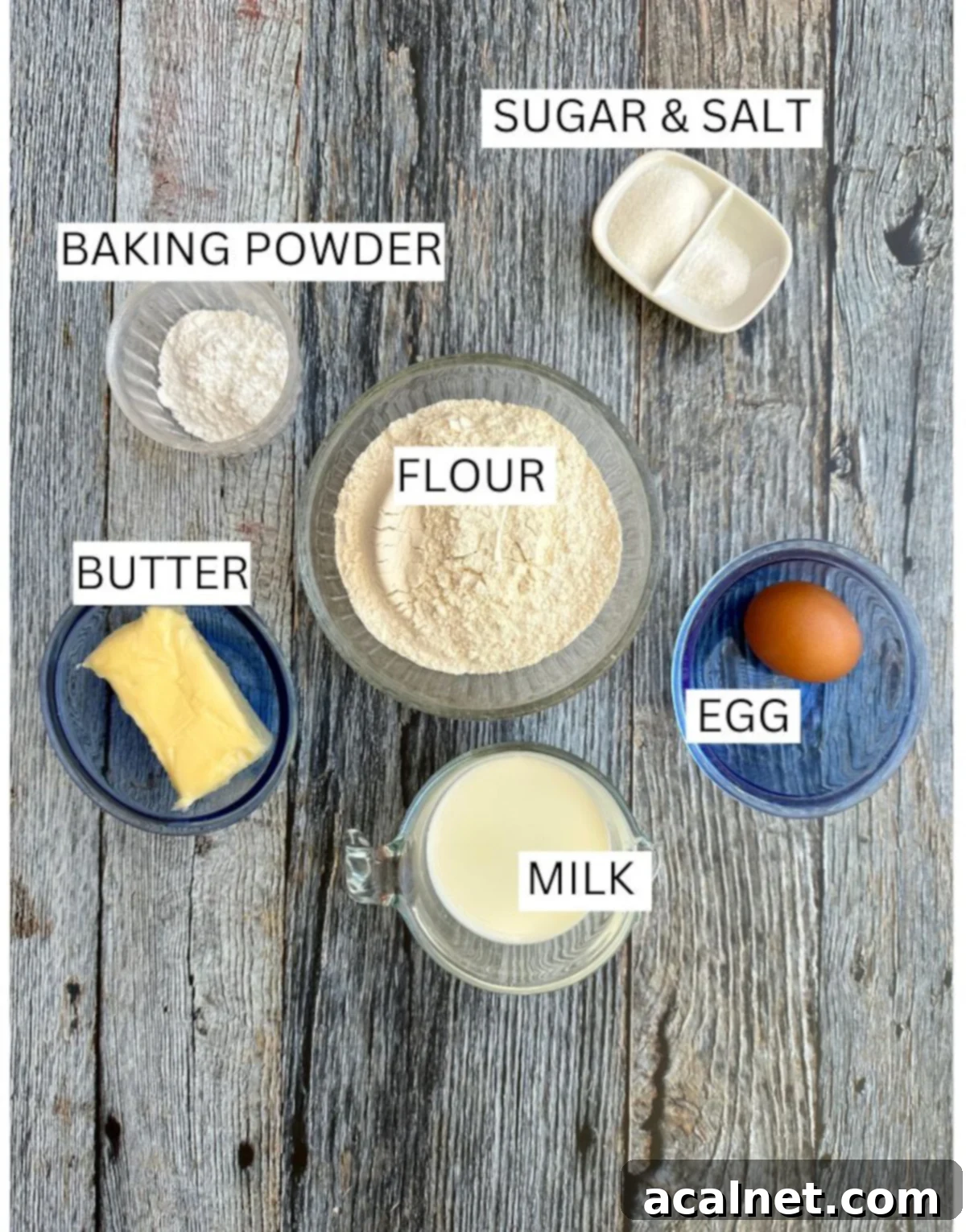 Homemade biscuit ingredients laid out on a rustic wooden table, including flour, butter, milk, and eggs.