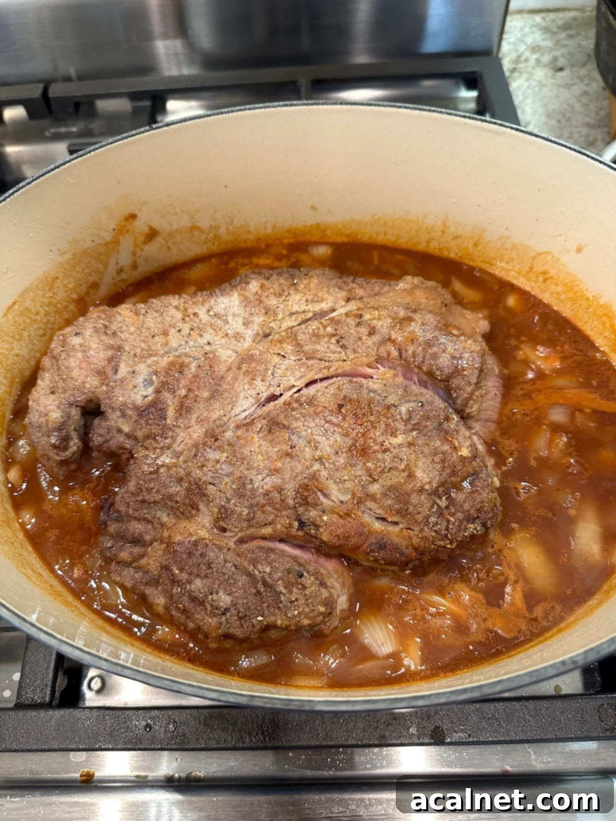 Pot roast in a Dutch oven with broth and vegetables.