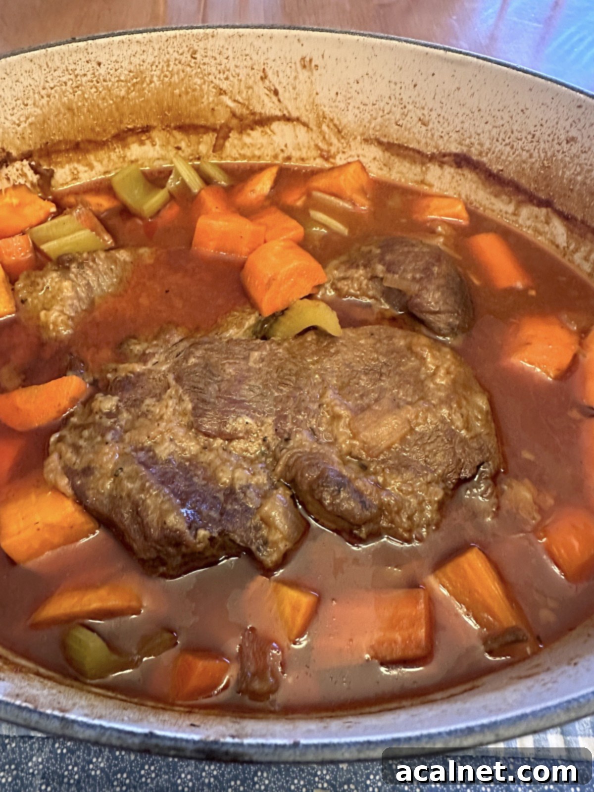 Baked pot roast in a Dutch oven with broth and vegetables.