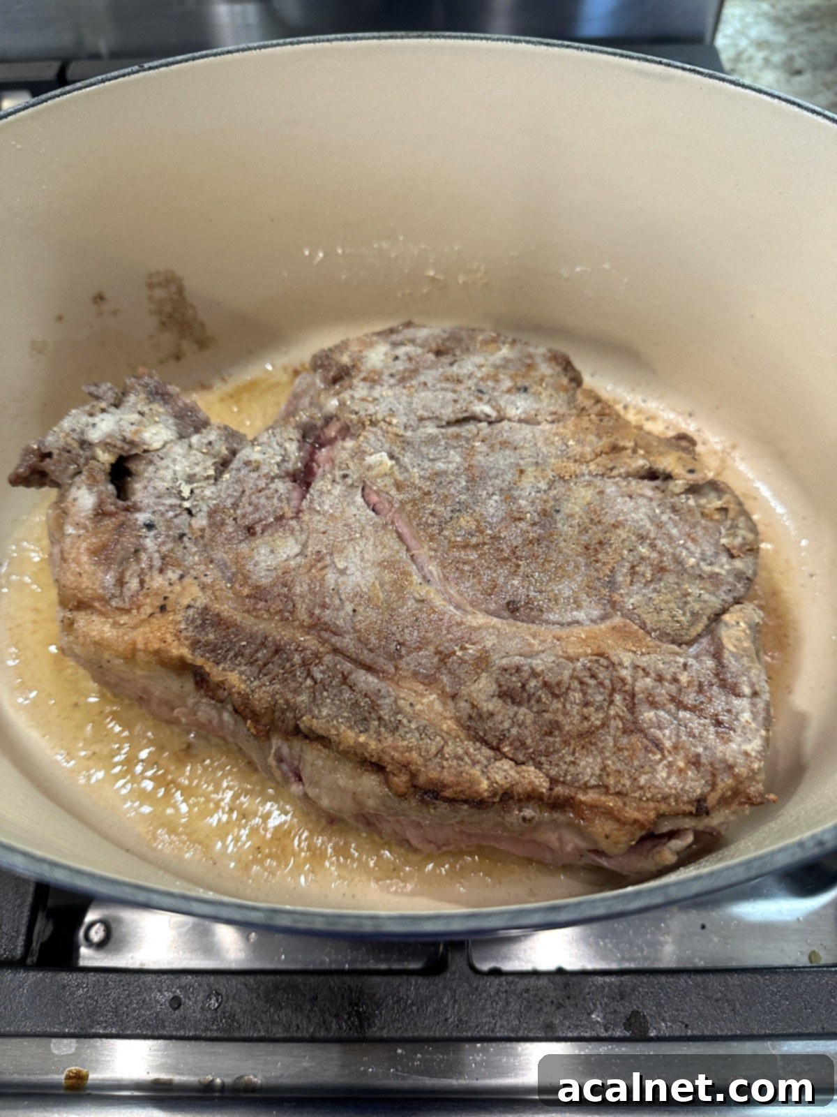Partially cooked pot roast in a Dutch oven on the stove.