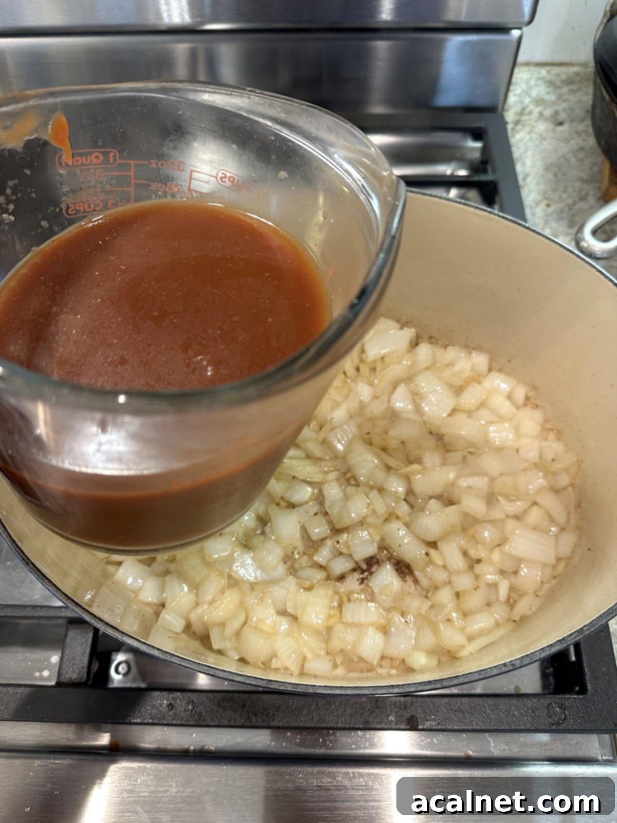 A measuring cup of liquid and a pan of cooked onions.