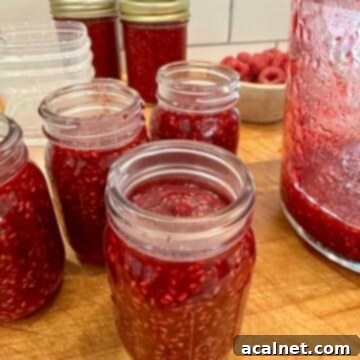 Small batch easy raspberry jam in clear jars on a rustic cutting board.